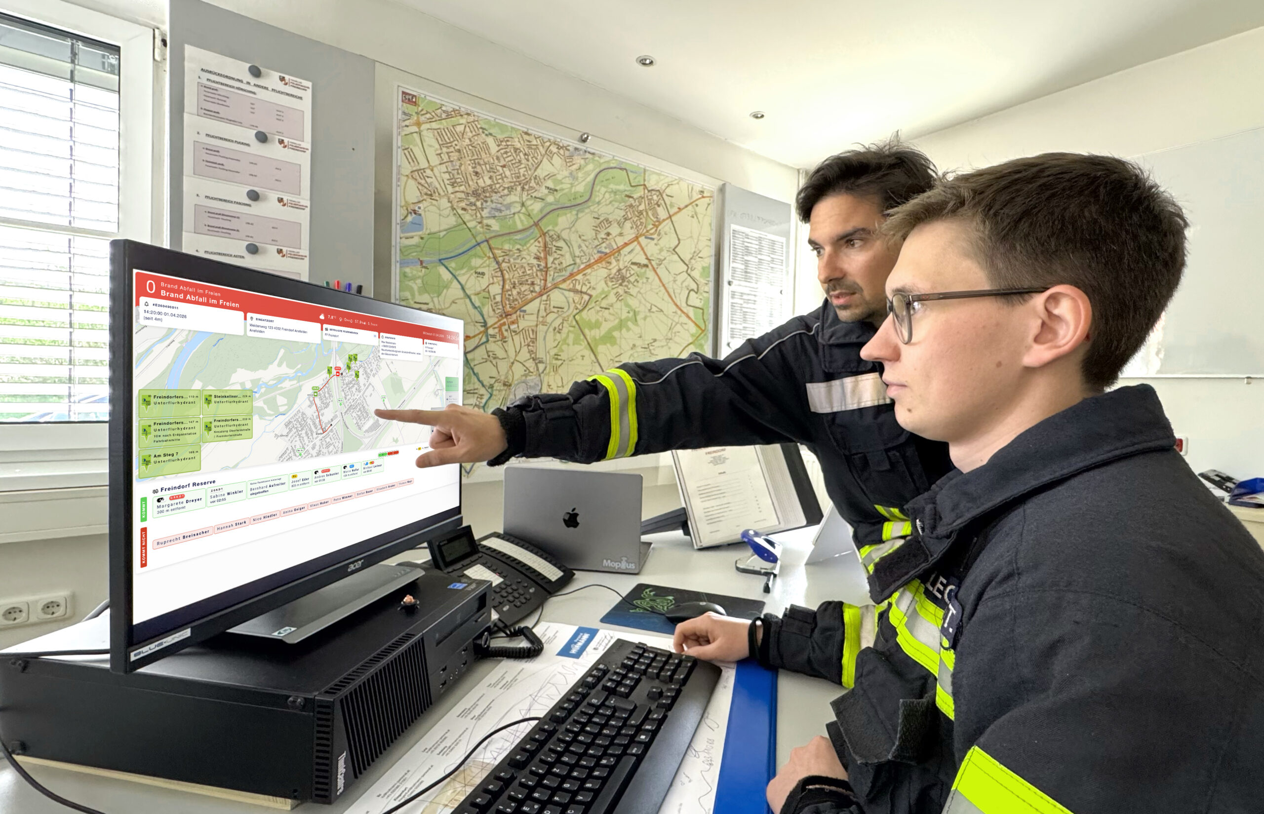 zwei Feuerwehrmänner in der Feuerwehrzentrale, die gerade das Feuerwehreinsatzinfos Dashboard am PC nutzen